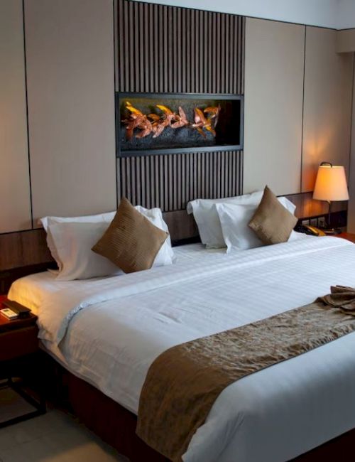 A neatly arranged hotel room with a double bed, decorative pillows, bedside tables with lamps, artwork, and curtains.