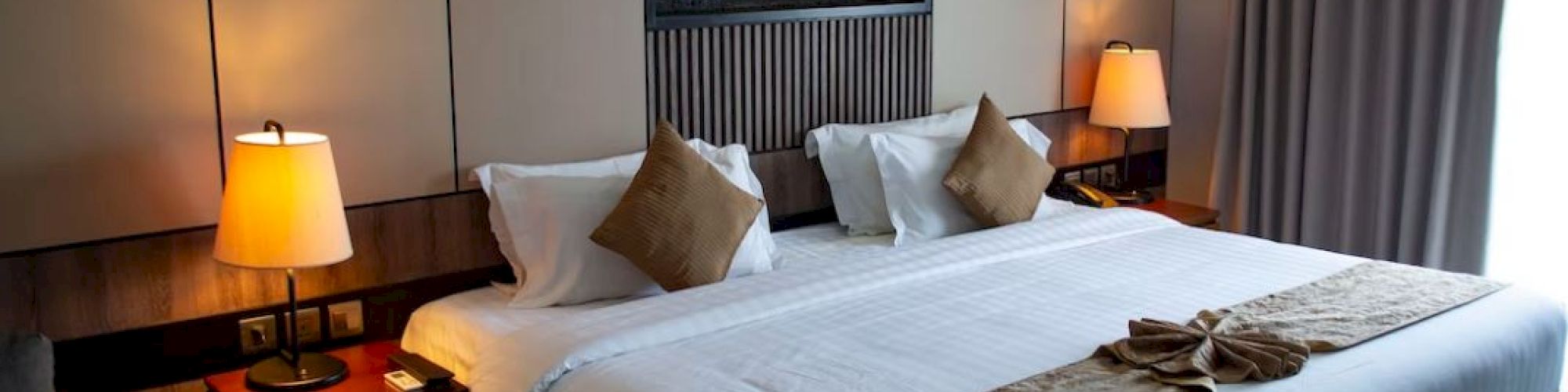 A cozy hotel room with a large bed, decorative pillows, bedside tables with lamps, and wall art above the bed.