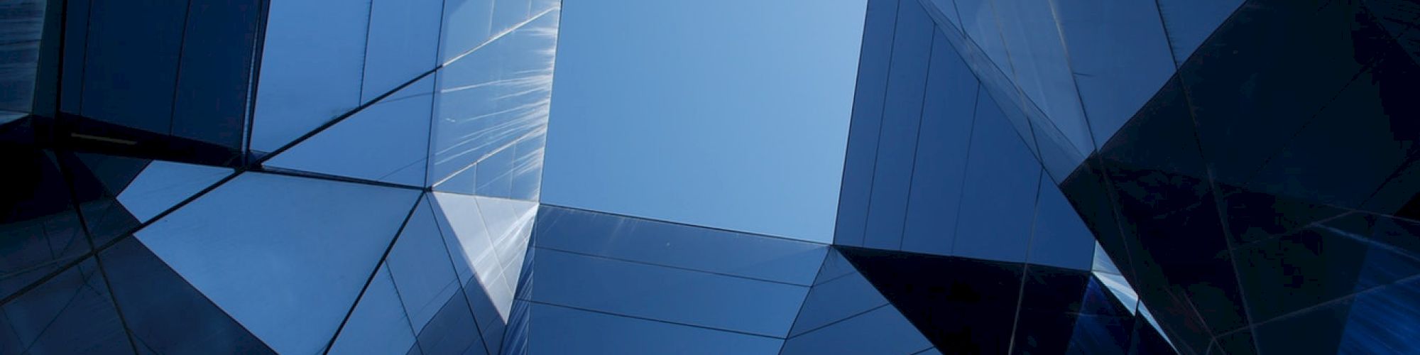 Geometric architectural design with mirrored surfaces reflects the sky, creating an abstract, kaleidoscope-like view.