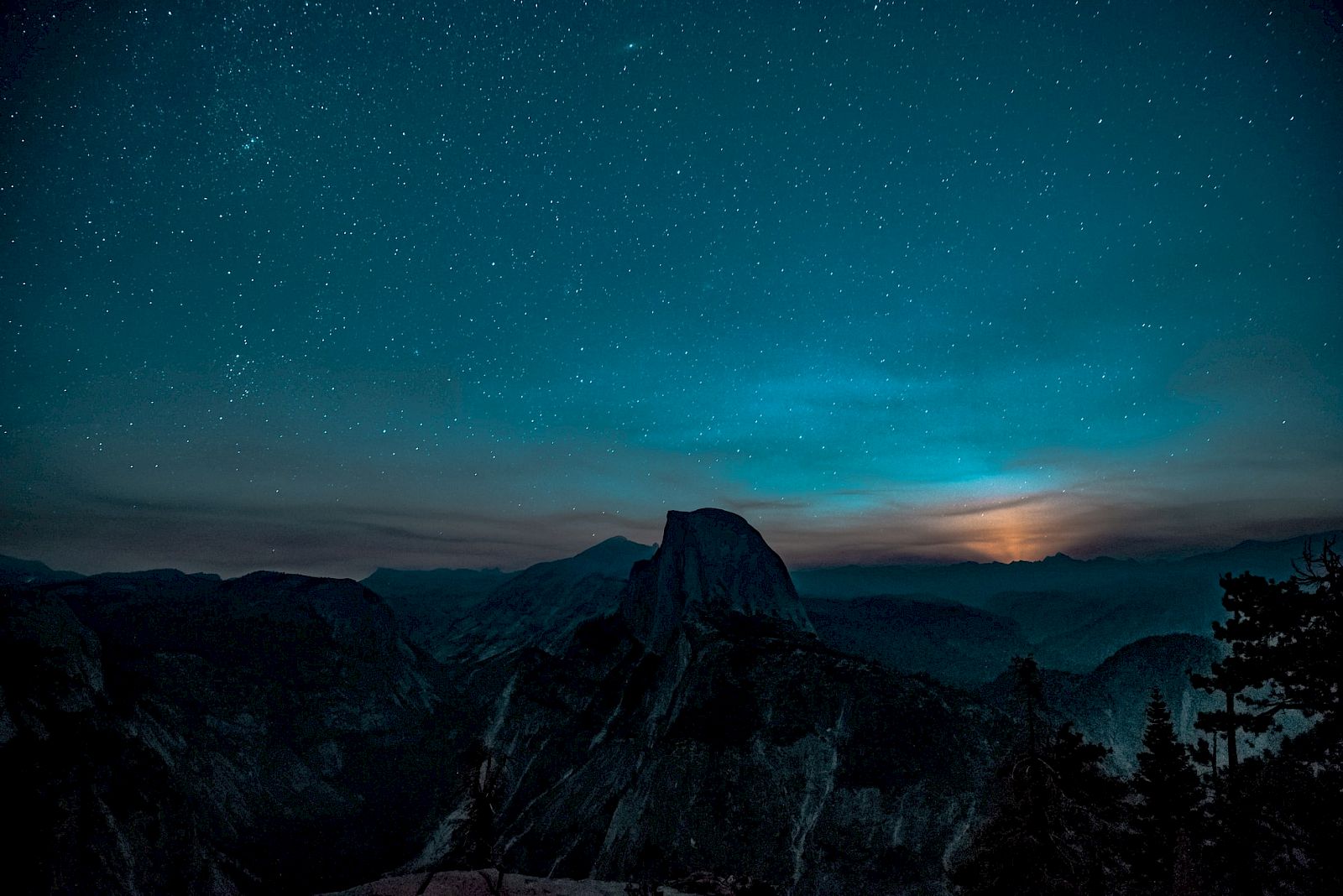 A starry night sky over a mountainous landscape with silhouettes and a dimly lit horizon completes the serene scene.