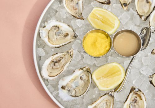 Oysters on ice with lemon wedges and two dipping sauces (yellow and beige) in small metal cups.