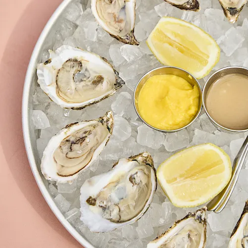Oysters on ice with lemon wedges and two dipping sauces (yellow and beige) in small metal cups.