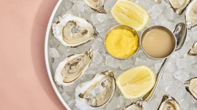 Oysters on ice with lemon wedges and two dipping sauces (yellow and beige) in small metal cups.
