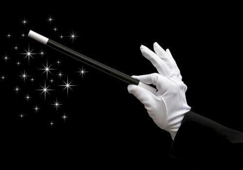 A gloved hand wields a wand over sparkling magic lights against a black background.