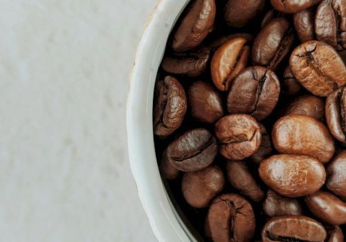 Roasted coffee beans are spilling from a white container.