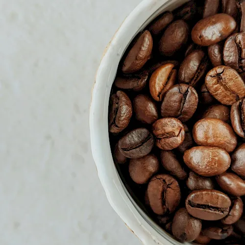 Roasted coffee beans are spilling from a white container.
