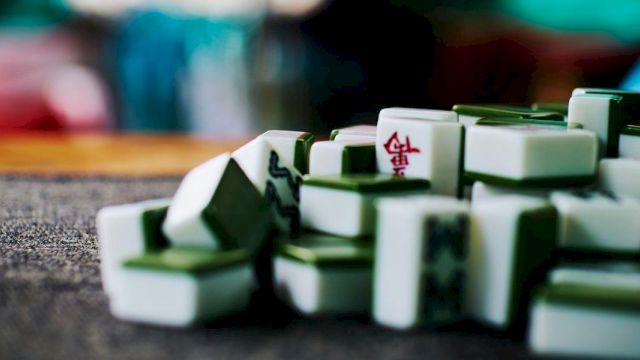 A close-up of Mahjong tiles scattered on a table, with a few marked backs in shallow depth of field.