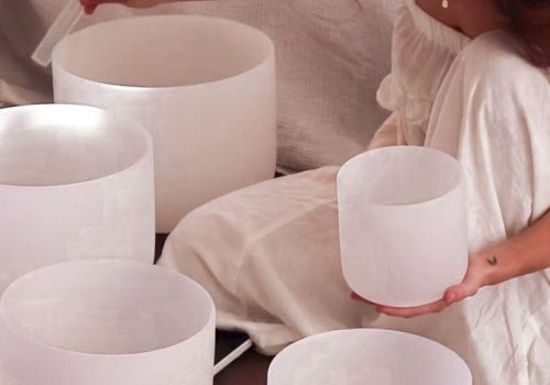 A woman in a white dress holds a white candle bowl while others sit on a table, creating a calm, minimalist vibe.