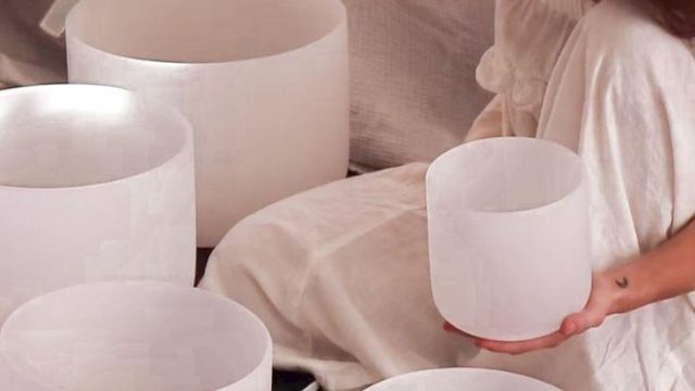 A woman in a white dress holds a white candle bowl while others sit on a table, creating a calm, minimalist vibe.