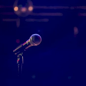 A studio-style microphone on a dark stage under colored lights, with soft bokeh in the background.