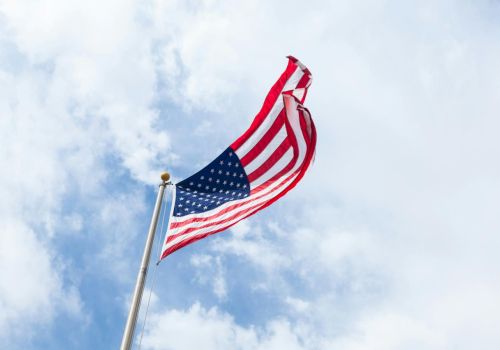 A large American flag waves on a pole against a bright blue sky with scattered clouds.