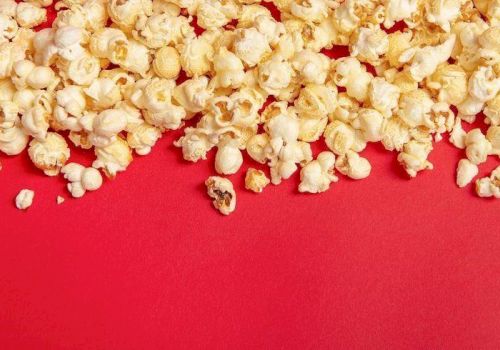 A pile of buttery popcorn kernels spilling across a red background.