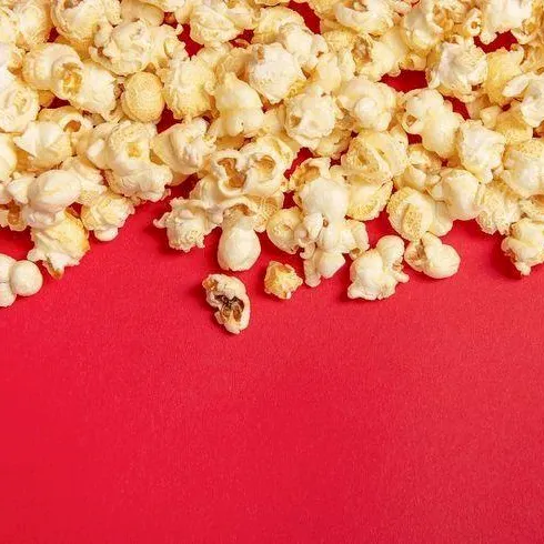 A pile of buttery popcorn kernels spilling across a red background.