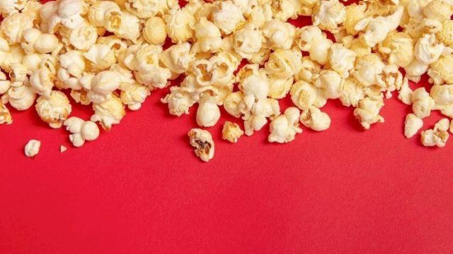 A pile of buttery popcorn kernels spilling across a red background.