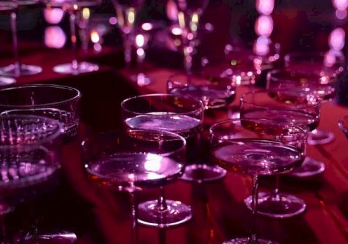 A row of empty champagne/cocktail glasses on a bar, lit in vivid purple-pink stage lighting.