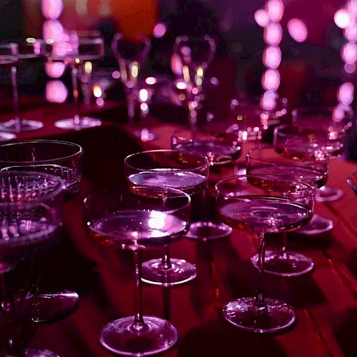 A row of empty champagne/cocktail glasses on a bar, lit in vivid purple-pink stage lighting.