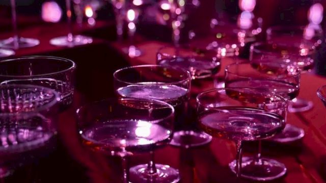 A row of empty champagne/cocktail glasses on a bar, lit in vivid purple-pink stage lighting.