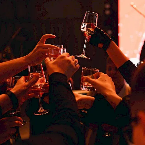 A group cheers with wine glasses in a warm, party-like setting, raising drinks together.