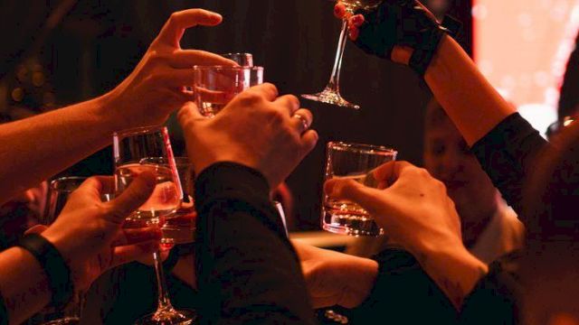 A group cheers with wine glasses in a warm, party-like setting, raising drinks together.