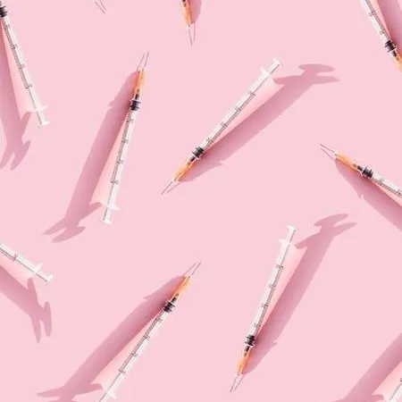 The image shows many syringes with needles scattered across a pink background.