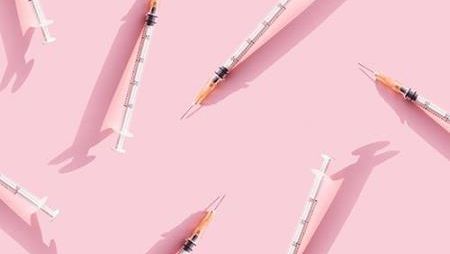 The image shows many syringes with needles scattered across a pink background.