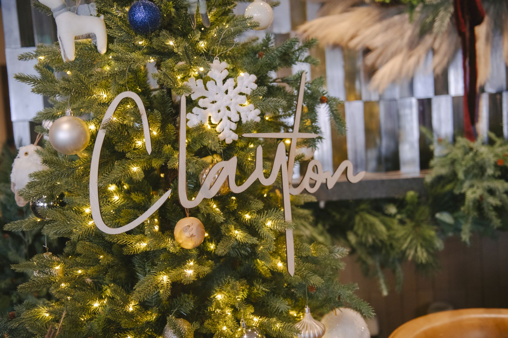 A decorated Christmas tree with warm lights, ornaments, and a &ldquo;Merry Christmas&rdquo; topper hanging in front of a festive background.