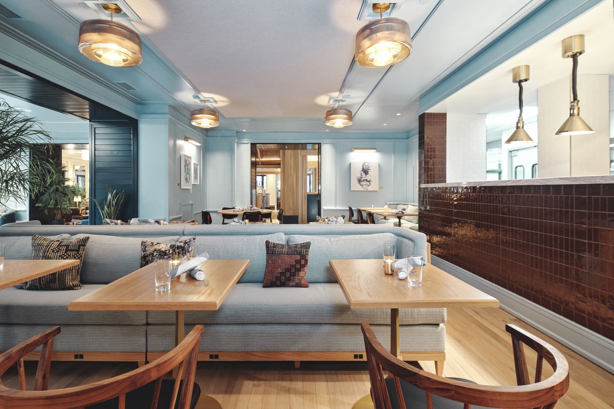 A stylish cafe interior with light wooden tables, pale blue seating, warm pendant lights, and a glossy dark tile wall, cozy and inviting.
