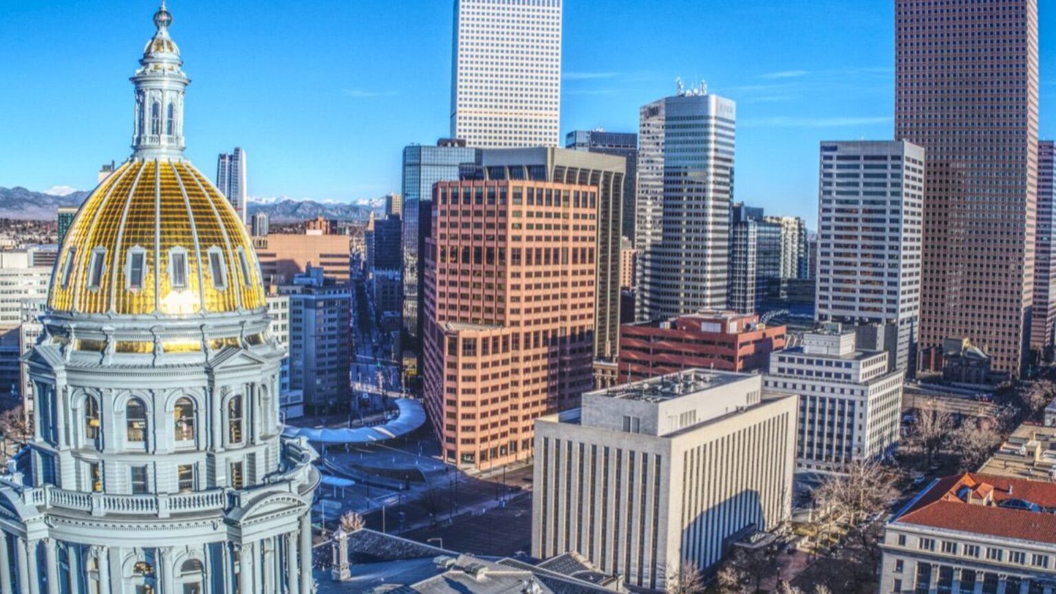 An urban skyline with a prominent golden-domed building, surrounded by modern high-rise structures, under a clear blue sky.