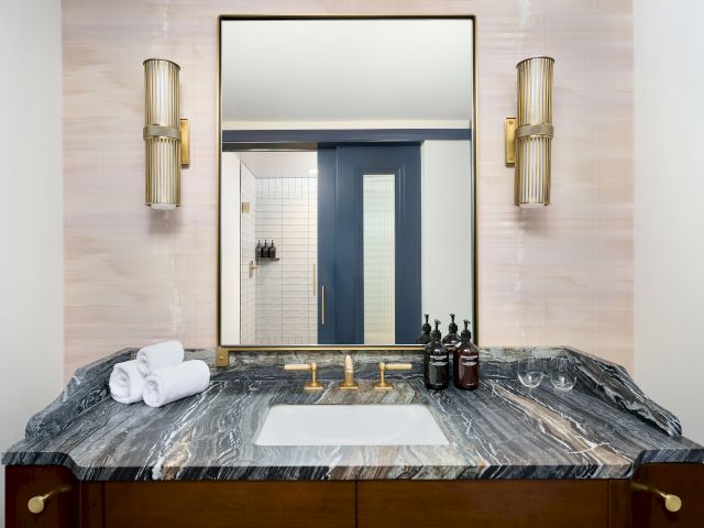 A bathroom vanity with a marble counter, a mirror, two wall lights, faucet, toiletries, and towels neatly arranged on the surface.