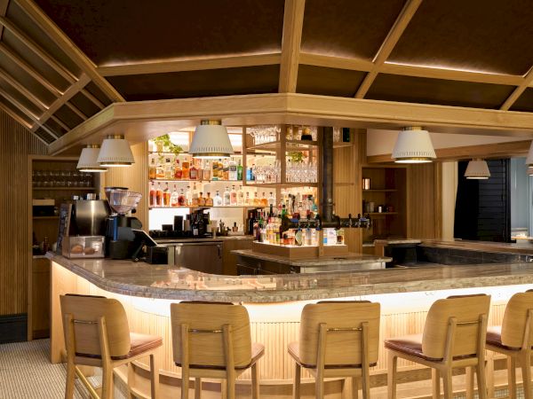 A stylish bar interior with a curved illuminated counter, wooden stools, warm lighting, and shelves stocked with bottles in the background, inviting ambiance.