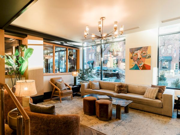 Cozy, stylish living room with beige sofas, a modern chandelier, plants, a large window, and art on the wall, inviting and warm.