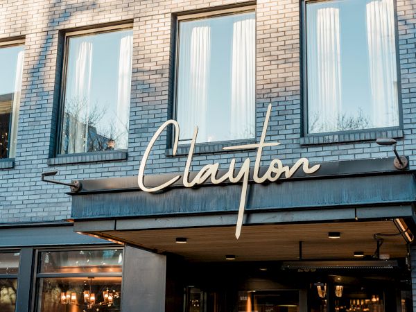 A storefront with a brick facade and a cursive sign reading &ldquo;Clayton&rdquo; above the entrance, reflecting a chic, urban vibe.