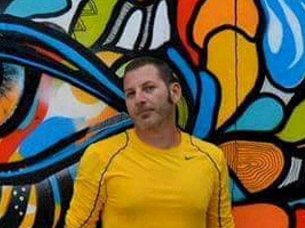 A person in a yellow shirt stands in front of a colorful graffiti-covered wall.