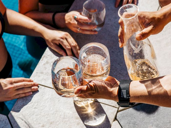 People by a poolside sharing drinks, holding glasses, and enjoying a sunny day together.