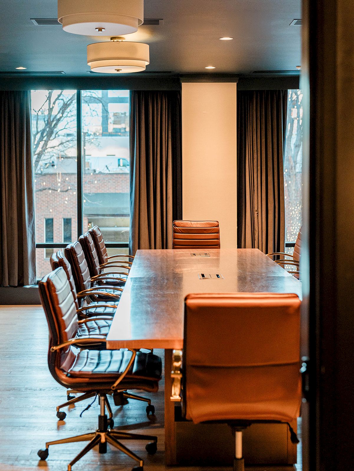 A modern conference room with a long wooden table, leather chairs, large windows, and warm lighting. 140 characters, ending with a period.