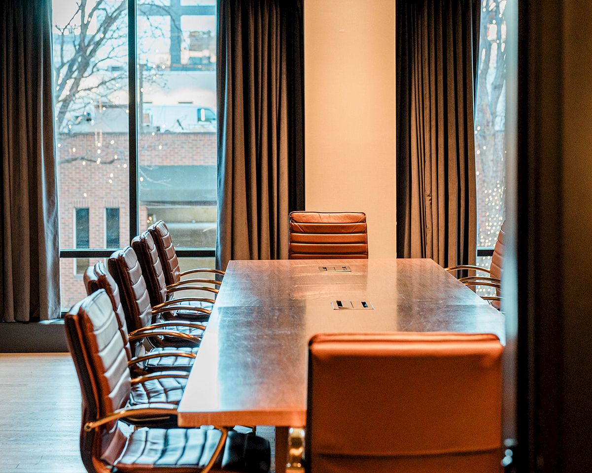 A modern conference room with a long wooden table, leather chairs, large windows, and warm lighting. 140 characters, ending with a period.