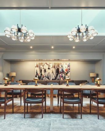 A spacious meeting room with a long table, chairs, modern chandeliers, artwork on the wall, and comfortable seating areas.