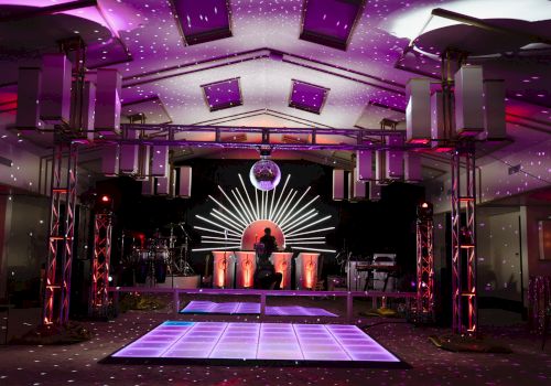 A vibrant dance floor with colorful lighting, a DJ booth, and speakers, creating a lively party atmosphere.