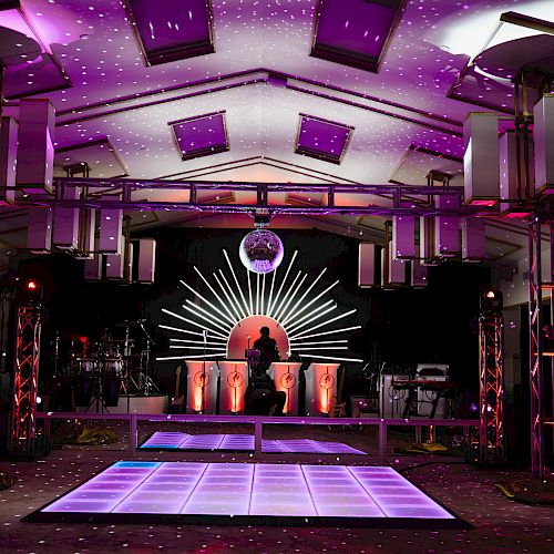 A vibrant dance floor with colorful lighting, a DJ booth, and speakers, creating a lively party atmosphere.