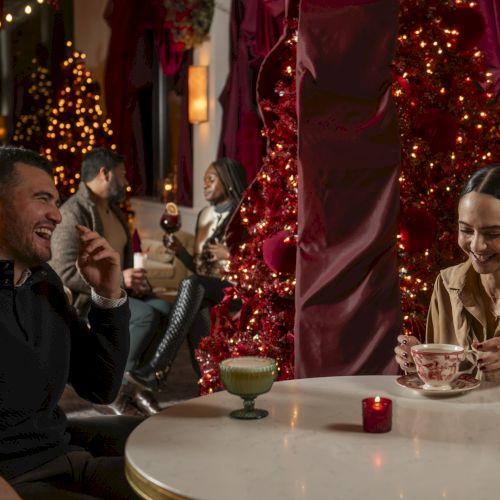 Two people chat and laugh at a cozy, warmly lit outdoor cafe decorated with lights and candles, sharing drinks and smiles.