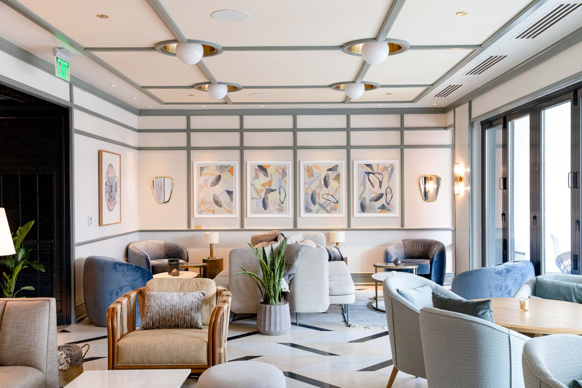 A chic lounge area with modern furniture, abstract art on the walls, and ample natural light from large windows.