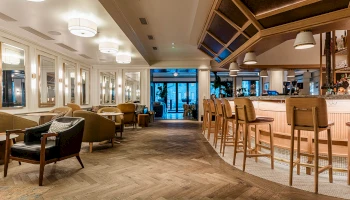 A stylish hotel lounge with warm lighting, comfortable seating, and a curved bar area; inviting, modern, and spacious, with a view toward the entrance.
