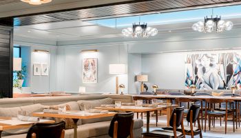 A stylish, airy dining area with light blue walls, long wooden tables, and mix-and-match chairs; modern art and warm lighting create a cozy, communal vibe.