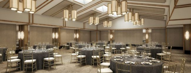 Elegant banquet hall with round tables, gray tablecloths, and gold chairs under modern pendant lights, ready for a formal event.