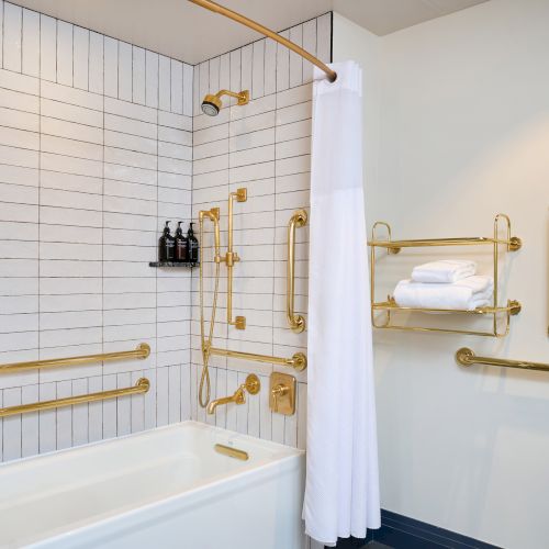 A bathroom with gold fixtures, a bathtub, a shower curtain, and white tiles. There are towel racks and wall-mounted shampoo bottles.