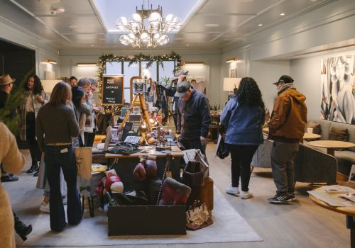 A group of people are browsing items displayed on a long table in a well-lit indoor space with modern decor.