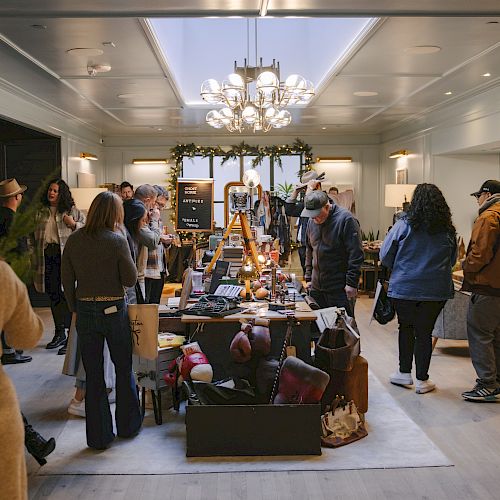 A group of people are browsing items displayed on a long table in a well-lit indoor space with modern decor.