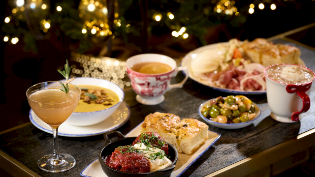 A festive feast: a table with assorted dishes, including a cocktail, soup, bread, salad, meats, vegetables, and a dessert, set under warm fairy lights.