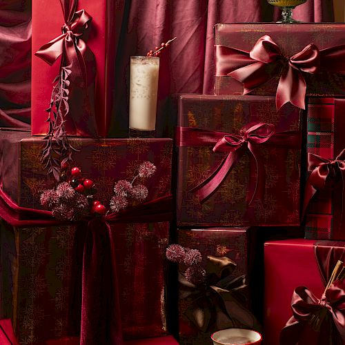 A stack of elegant red gift boxes with ribbons, velvet background, a candle, cup, and berries, all arranged festive and luxurious.