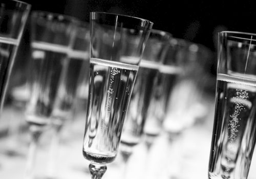 A row of elegant champagne flutes stands upright in a blurred setting, showcasing their tall stems and bubbly contents, evoking a celebratory toast.